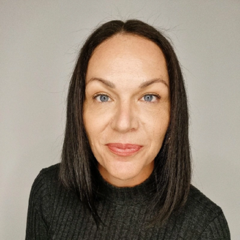 Woman with straight dark hair and blue eyes against plain background